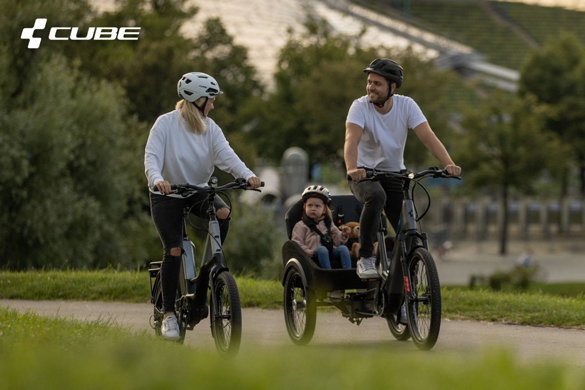 Mamma e papà pedalano in sella a due ebike portando con sé la figlia, posizionata nel box posteriore della nuova eCargo di Cube